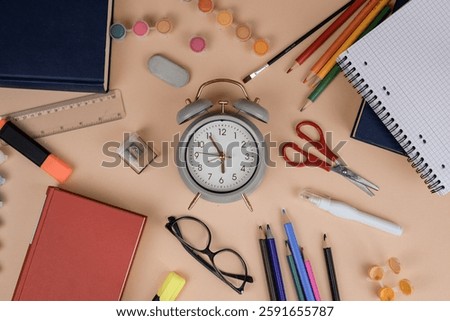 An alarm clock is placed on a table along with various school supplies