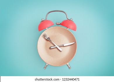 Alarm clock and plate with cutlery . Concept of intermittent fasting, lunchtime, diet and weight loss