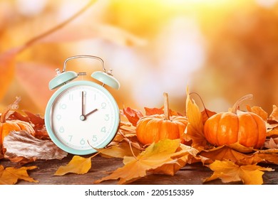 Alarm clock, pumpkins and autumn leaves on table outdoors - Shutterstock ID 2205153359