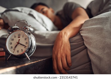 Alarm clock, relax and man sleeping in the bed of his modern apartment in the morning. Lazy, resting and closeup of a timer bell with a male person taking a nap and dreaming in bedroom at his home.