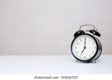 An alarm clock showing 7 o'clock standing on a white table with copy space, everyday shedule and morning wake up concept