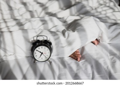 Alarm clock showing 7 oclock on the bed with sleeping person feet on blanket in the morning