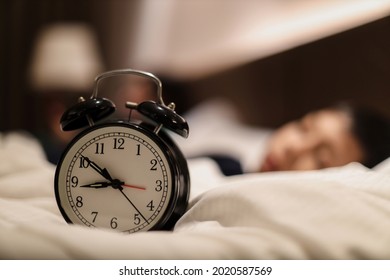 Alarm clock showing 9 o'clock pm with blurry background of boy sleeping on the bed