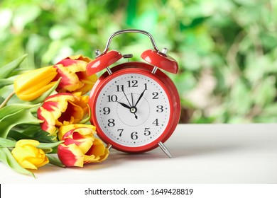 Alarm Clock And Spring Flowers On White Wooden Table. Time Change Concept