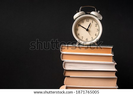 The alarm clock stands on a stack of books on a black background. Training concept and preparation for work