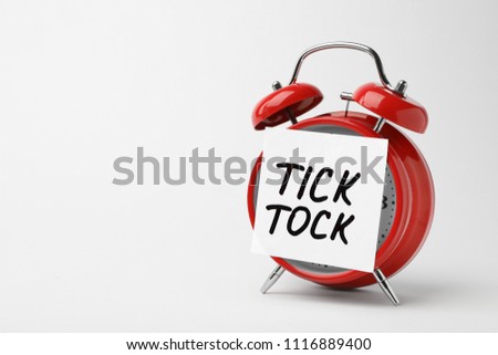 Alarm clock and sticky note with words TICK TOCK on white background. Time concept