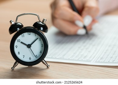 Alarm Clock For A Student Writing Exams, Taking An Exam Room With A Pencil Holding On An Optical Form Of A Standardized Test With Answers