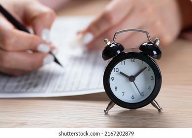 Alarm Clock For A Student Writing Exams, Taking An Exam Room With A Pencil Holding On An Optical Form Of A Standardized Test With Answers