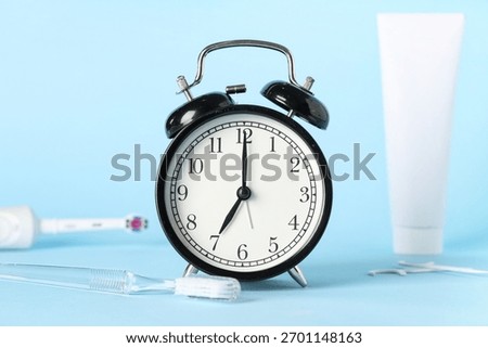 Alarm clock, toothpaste and toothbrushes on blue background
