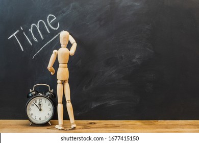 Alarm clock and wooden figure writes text "time" on the chalkboard.