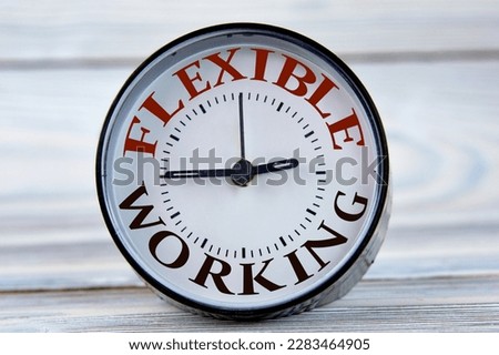 Alarm clock with words FLEXIBLE WORK on light wooden background close-up. Business concept