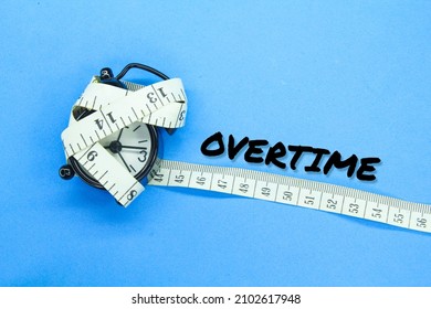 the alarm clock is wrapped with measuring tape with the word overtime - Shutterstock ID 2102617948