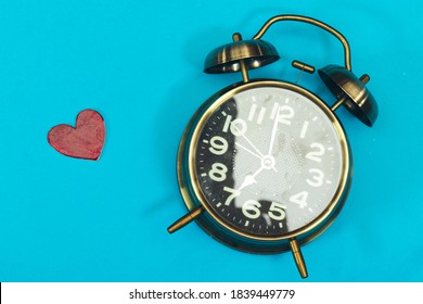alarm showing 7 o'clock with wooden heart isolated on blue
