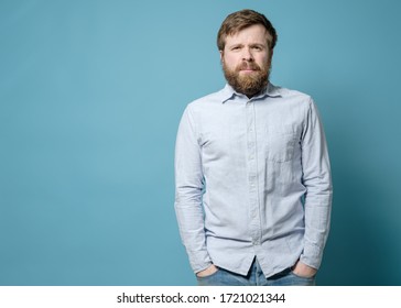 Alarmed Caucasian Man With A Shaggy Beard And An Overgrown Hairstyle Stands With Hands In Jeans Pockets. Copy Space.