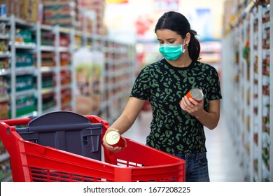 Alarmed Female Wears Medical Mask Against Coronavirus While Grocery Shopping In Supermarket Or Store- Health, Safety And Pandemic Concept - Young Woman Wearing Protective Mask  And Stockpiling Food