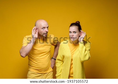 Alarmed man and woman in yellow t-shirts overhear someones conversations and stare fearfully into the camera. Studio.