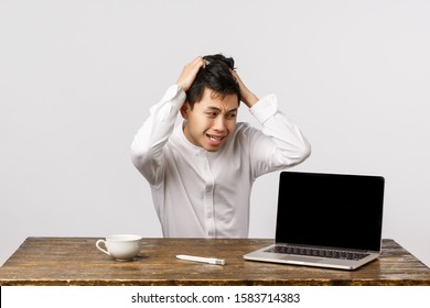 Alarmed And Panicking Chinese Guy Pulling Hair From Head Sitting Troubled And Distressed, Having Huge Problem, Staring At Laptop With Anxious, Nervous Expression, Sitting Office White Background