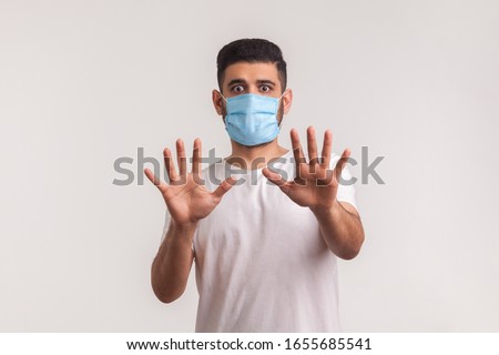 Alarming scared panicking man in hygienic mask gesturing stop, afraid of coronavirus infection, respiratory illnesses such as flu, 2019-nCoV, Covid-19, ebola. indoor shot isolated on white background