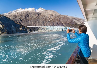 Alaska cruise tourist taking photo of Glacier Bay. Ship passenger on balcony looking at view taking smartphone pictures of Margerie glacier from boat. Woman using phone app on travel vacation.