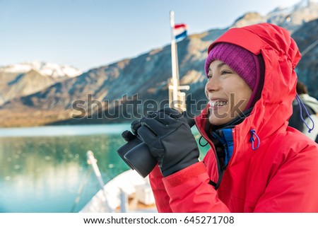 Alaska cruise travel woman looking at wildlife with binoculars. Tourist at Alaska Glacier Bay on ship. Woman on vacation looking at nature landscape enjoying cruising famous tourist destination.