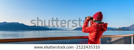 Alaska Glacier Bay cruise ship passenger looking at Alaskan mountains in binoculars exploring Glacier Bay National Park, USA. Woman on travel Inside Passage enjoying view. Vacation adventure banner.
