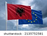 Albania and EU flag together next to each other on a flagpole. Albanian flag in front of a European Union flag on a dramatic stormy sky background