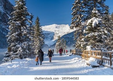 Alberta, Canada - OCT 10 2020 : Tourists sightseeing at Lake Louise in early winter sunny day morning. Clear blue sky, snow capped mountains in background. Beautiful landscape in Banff National Park.