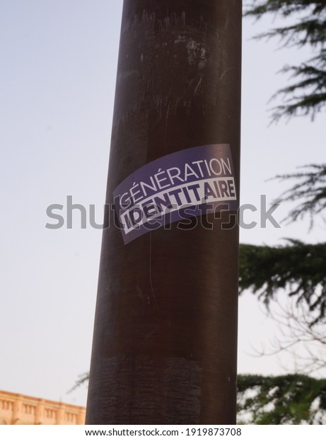 Albi, France - Feb. 2021 - A blue and white sticker\
from Génération Identitaire, a right-wing youth movement opposing\
the migratory invasion and the Islamization of Europe, pasted on a\
lamp post pole