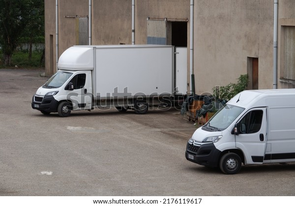 Albi, France - July 2022 - White Citroën and\
Peugeot moving vans in reverse, unloading position, with their\
doors open, in front of the sliding doors of a storage unit used as\
a furniture repository