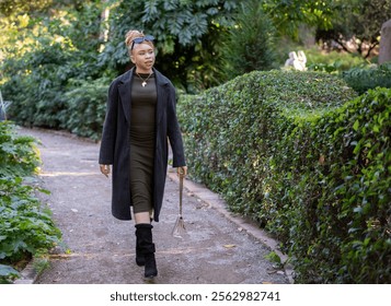 Albino african american model walking in a park wearing a gray coat, green dress, sunglasses and a necklace with the shape of Africa while holding a purse - Powered by Shutterstock