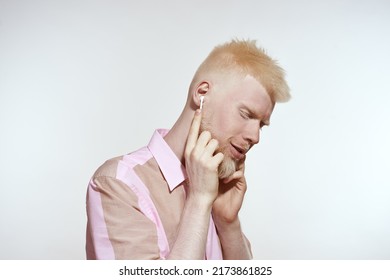 Albino Caucasian Guy Choosing And Listening Music In Wireless Earphones. Young Bearded Blonde Man Of Generation Z With Closed Eyes Wearing T-shirt. Isolated On White Background In Studio. Copy Space