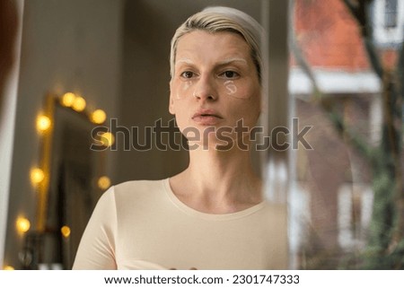 Albino woman applying eye patches in bathroom while looking at the mirror