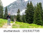 Albion Basin, Utah pine trees and man standing on summer dirt road trail in 2019 in Wasatch mountains with rocky snowy Devil