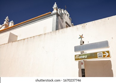 Albufeira, Algarve, Portugal - 6 March 2020: Information Sign With Museum Caption Standing On The Background Of Wall Of Traditional Portuguese Church Building.
