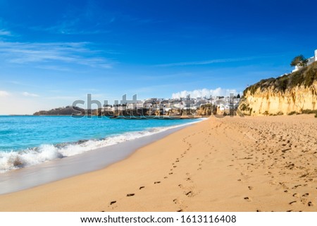 Albufeira resort village, popular touristic destination in Algarve, Portugal. Waves crashing against wide sandy beach Praia de Albufeira and view over cliffs and white houses in the old town