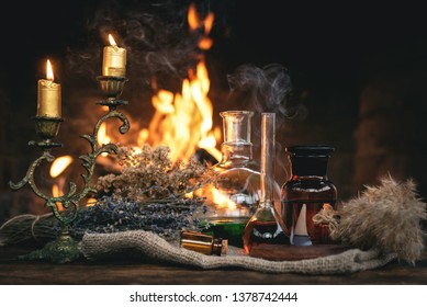 Alchemist or witch doctor table. Magic potion bottles and dried herbs on a table on a burning fire background. Witchcraft concept.