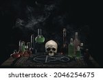 Alchemist , wizard or witch workplace. The altar. Magic potions and skull on the wooden table. Dark smoky background. Witchcraft and Halloween concept.
