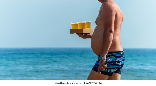 Alcohol abuse fat man with full beer copy space, full man with a big belly carries a tray with beer on beach close-up