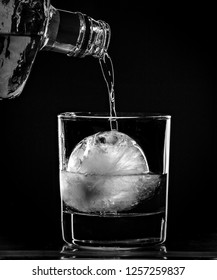 Alcohol Being Poured Into A Cocktail Glass With A Large Round Ice Ball.