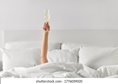 alcohol, celebration and morning concept - hand of young woman lying in bed with champagne glass