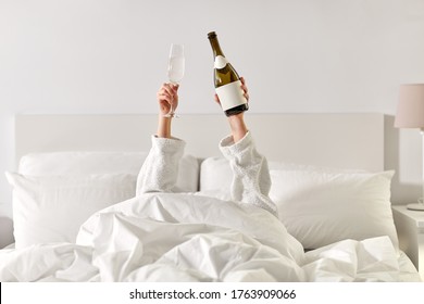 Alcohol, Celebration And Morning Concept - Hands Of Young Woman In Hotel Robe Lying In Bed With Champagne Glass And Bottle