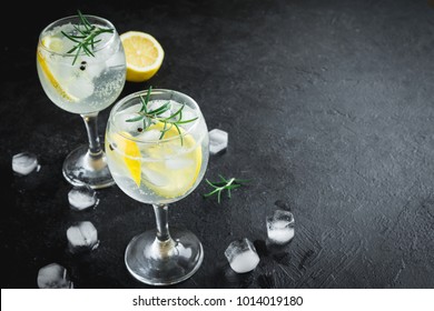 Alcohol drink (gin tonic cocktail) with lemon, rosemary and ice on rustic black stone table, copy space, top view. Iced drink with lemon and herbs. - Shutterstock ID 1014019180