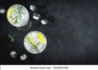 Alcohol drink (gin tonic cocktail) with lemon, rosemary and ice on rustic black stone table, copy space, top view. Iced drink with lemon and herbs. - Shutterstock ID 1014019183