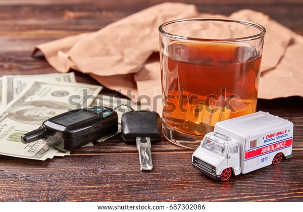 Alcohol drink\
and keys. Money, car keys, glass of whiskey, ambulance on wooden\
background. Drunk driving\
concept.