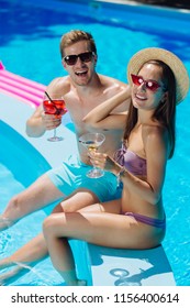 Alcohol Drinks. Modern Stylish Couple Wearing Sunglasses Drinking Alcohol Drinks Sitting Near Pool