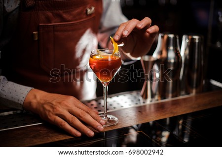 alcohol drinks, people and luxury concept - bartender with glass and lemon peel preparing cocktail at bar