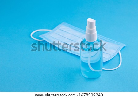 Alcohol gel hand sanitizer and disposable hygienic mask on blue background with copy space. Bottle of hand sanitizer, antimicrobial liquid spray, germ prevention or antibacterial hygiene, copy space.