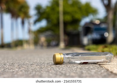 Alcohol nip bottle laying on sidewalk next to public park