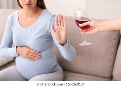 Alcohol In Pregnancy. Unrecognizable Expectant Lady Gestring Stop To Offered Glass Of Wine Sitting On Couch At Home. Cropped
