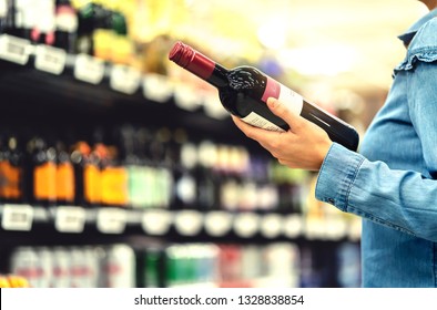 Alcohol Shelf In Liquor Store Or Supermarket. Woman Buying A Bottle Of Red Wine And Looking At Alcoholic Drinks In Shop. Happy Female Customer Choosing Merlot Or Sangiovese. Shopping Spirits Concept.